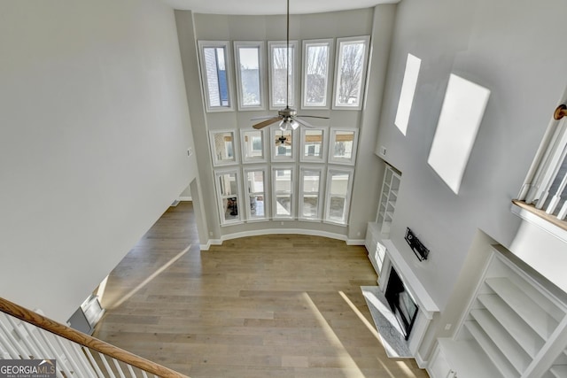 unfurnished living room with a fireplace, a towering ceiling, baseboards, a ceiling fan, and light wood-type flooring