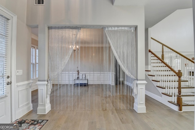 entrance foyer with visible vents, wainscoting, stairway, wood finished floors, and a chandelier