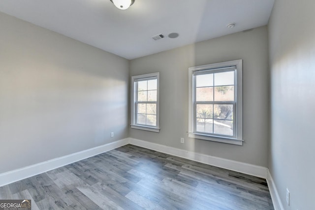 spare room with wood finished floors, visible vents, and baseboards