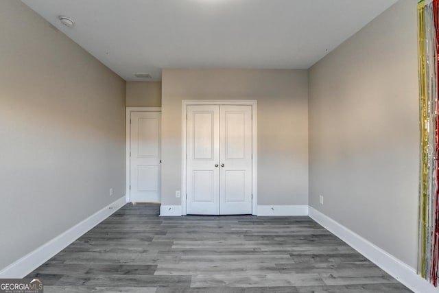 unfurnished bedroom featuring a closet, visible vents, baseboards, and wood finished floors