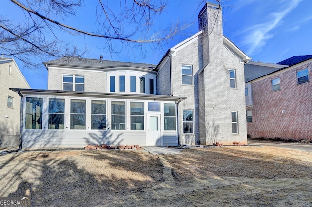 rear view of property with brick siding, a chimney, and a sunroom