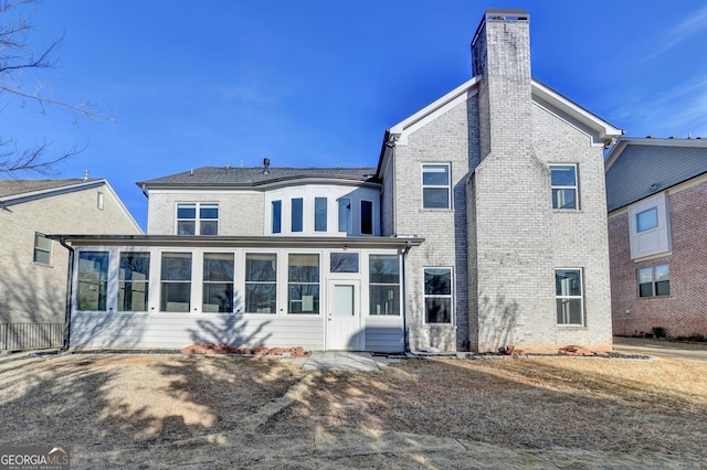 rear view of house with a sunroom, a chimney, and brick siding