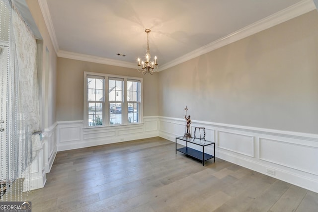 spare room featuring visible vents, wood finished floors, an inviting chandelier, crown molding, and a decorative wall