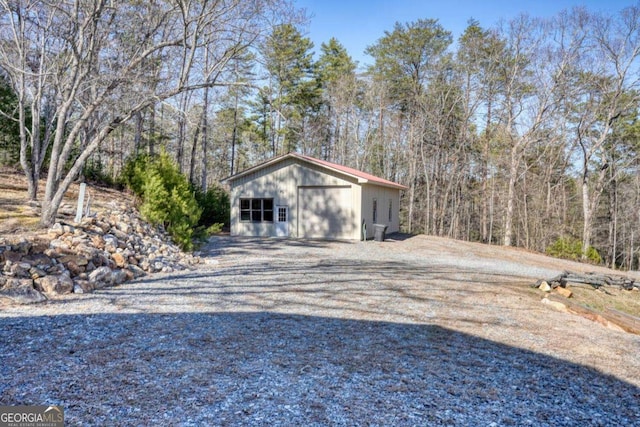 detached garage with gravel driveway and a forest view