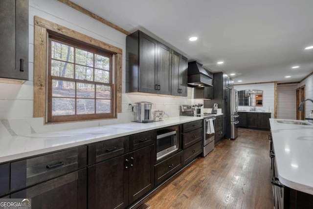 kitchen featuring dark wood finished floors, custom range hood, appliances with stainless steel finishes, light stone countertops, and a sink