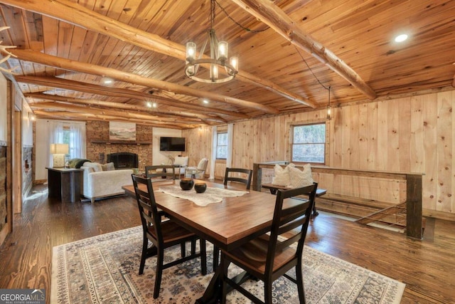 dining space with dark wood-style floors, a wealth of natural light, beam ceiling, and a stone fireplace