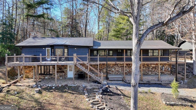 rear view of house featuring a deck, stone siding, metal roof, and stairway