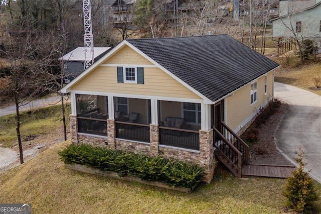 exterior space featuring stone siding, roof with shingles, and a sunroom