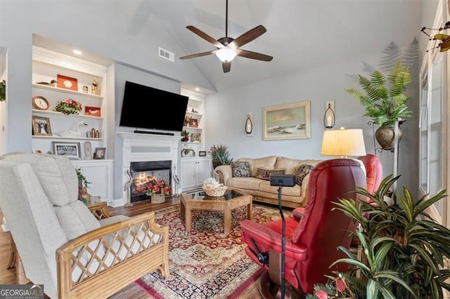 living room with lofted ceiling, ceiling fan, a warm lit fireplace, visible vents, and built in features