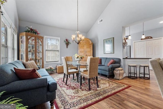 dining space with high vaulted ceiling, wood finished floors, visible vents, and an inviting chandelier