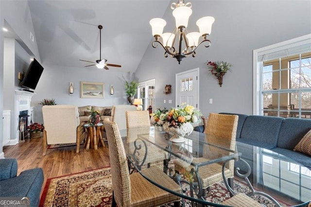 dining room featuring lofted ceiling, ceiling fan with notable chandelier, wood finished floors, and a glass covered fireplace