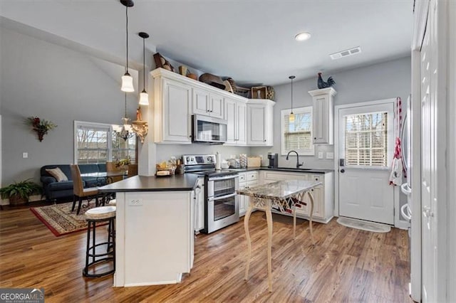 kitchen with stainless steel appliances, dark countertops, visible vents, wood finished floors, and a peninsula