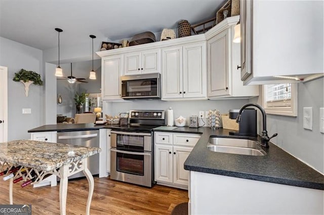 kitchen featuring stainless steel appliances, wood finished floors, a sink, white cabinets, and dark countertops