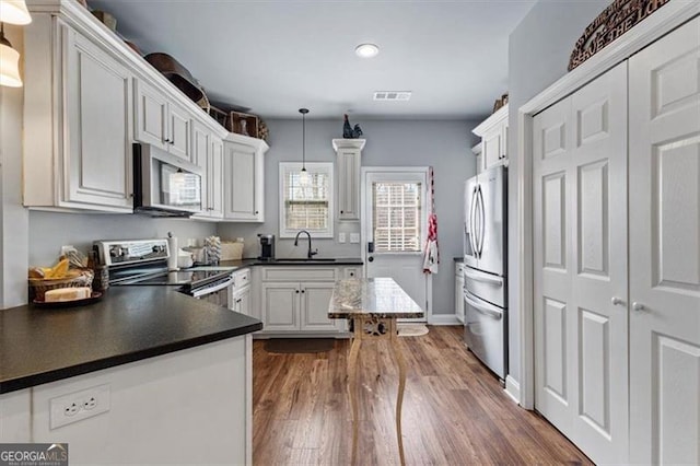 kitchen with stainless steel appliances, dark wood-style flooring, a sink, visible vents, and dark countertops