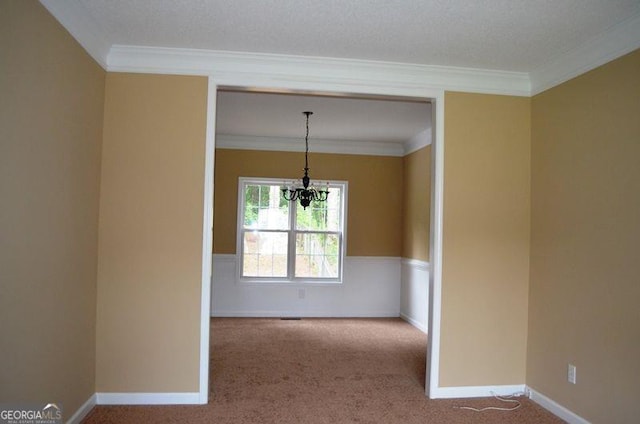 carpeted empty room with ornamental molding, baseboards, and an inviting chandelier