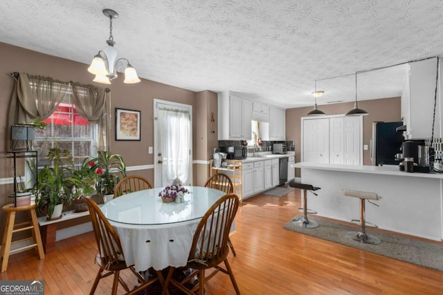 dining area featuring light wood-type flooring, a textured ceiling, and an inviting chandelier