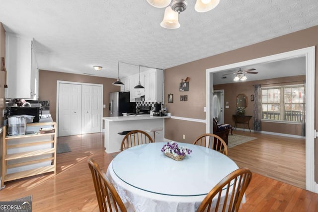 dining space with a ceiling fan, baseboards, a textured ceiling, and light wood finished floors