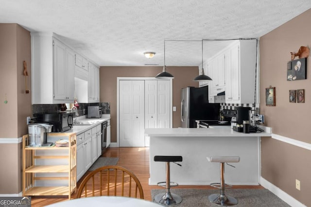 kitchen with a peninsula, a sink, white cabinetry, light countertops, and black appliances