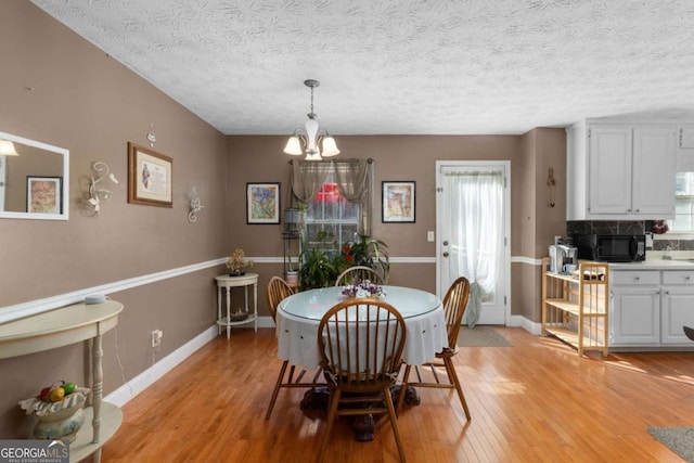 dining area featuring baseboards, a textured ceiling, light wood-type flooring, and an inviting chandelier