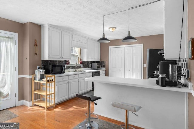 kitchen featuring a peninsula, light countertops, black appliances, white cabinetry, and a sink