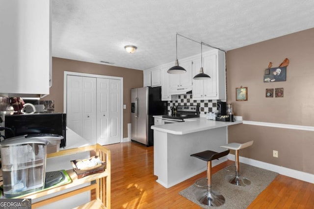 kitchen with under cabinet range hood, a peninsula, white cabinetry, appliances with stainless steel finishes, and backsplash