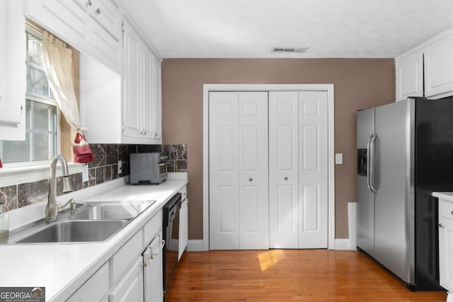 kitchen with black dishwasher, stainless steel fridge, visible vents, white cabinets, and a sink