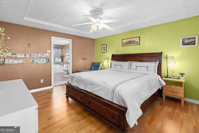 bedroom featuring a textured ceiling, connected bathroom, light wood-style flooring, and baseboards