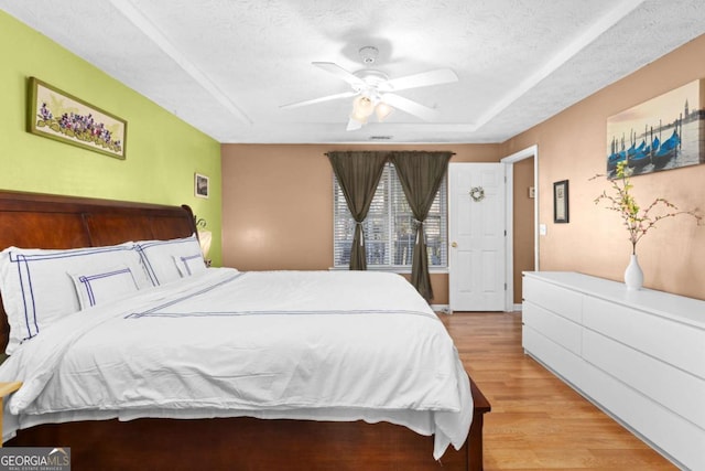 bedroom featuring a tray ceiling, ceiling fan, light wood-style flooring, and a textured ceiling