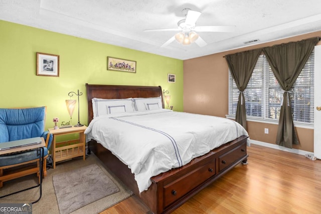 bedroom featuring a ceiling fan, visible vents, baseboards, and wood finished floors