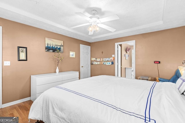 bedroom featuring a tray ceiling, ceiling fan, a textured ceiling, light wood-type flooring, and baseboards