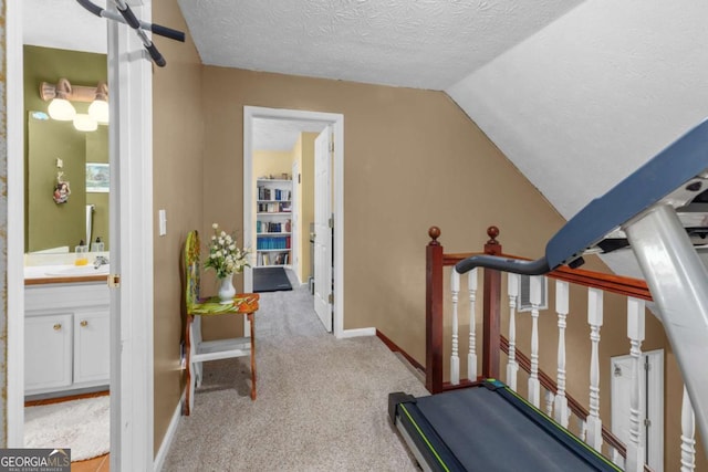 workout area featuring baseboards, carpet, vaulted ceiling, a textured ceiling, and a sink