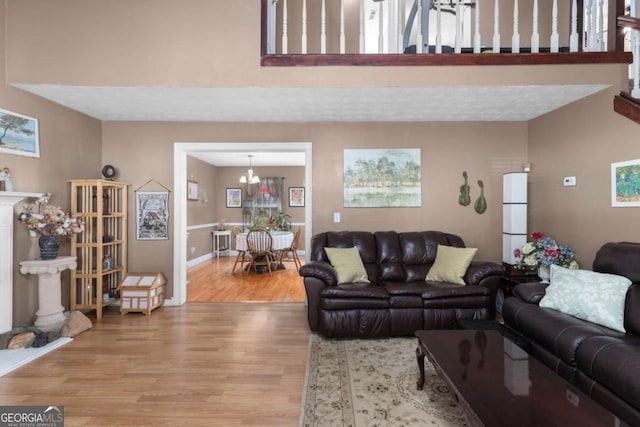 living area featuring light wood-style floors, baseboards, a fireplace with raised hearth, and a high ceiling