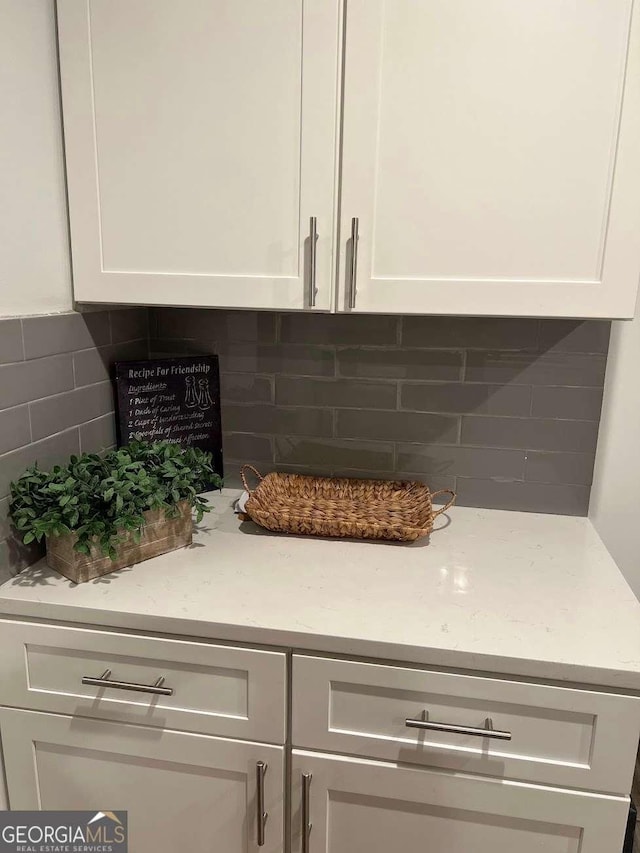 room details featuring tasteful backsplash, white cabinets, and light stone counters