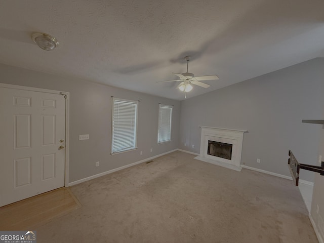 unfurnished living room featuring lofted ceiling, a glass covered fireplace, ceiling fan, a textured ceiling, and baseboards