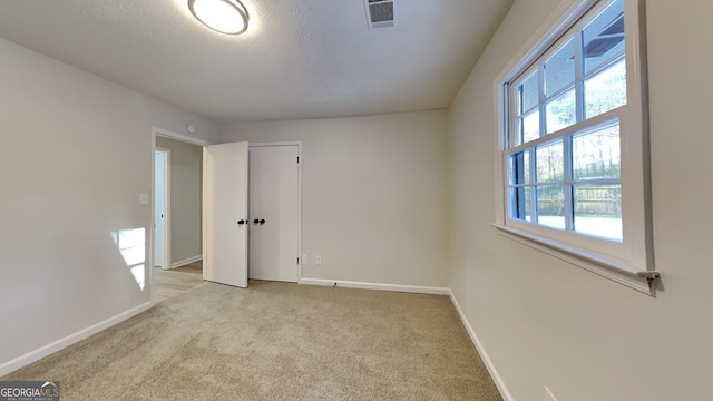 unfurnished bedroom featuring light carpet, baseboards, visible vents, a textured ceiling, and a closet