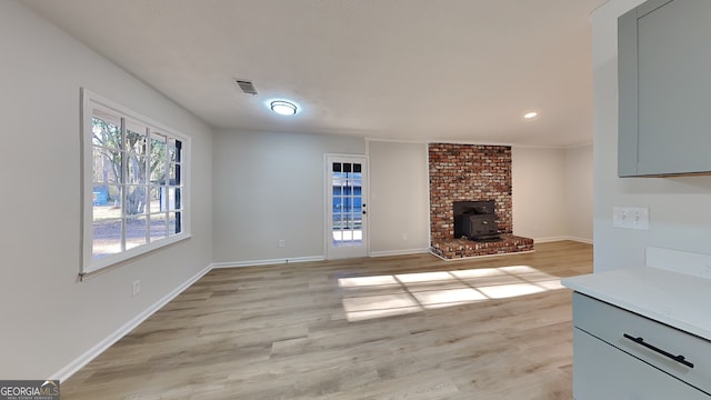 unfurnished living room with a wood stove, light wood-style flooring, visible vents, and baseboards