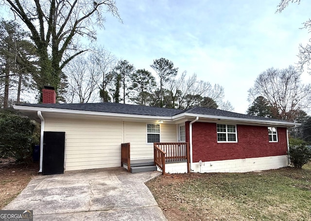 ranch-style house with roof with shingles, a chimney, and brick siding