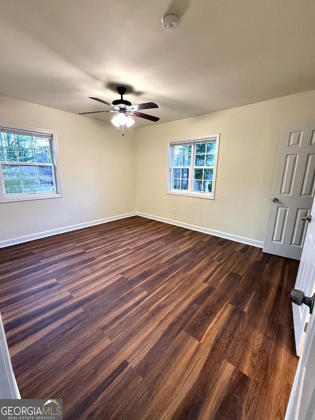 empty room with a healthy amount of sunlight, ceiling fan, baseboards, and dark wood-style flooring