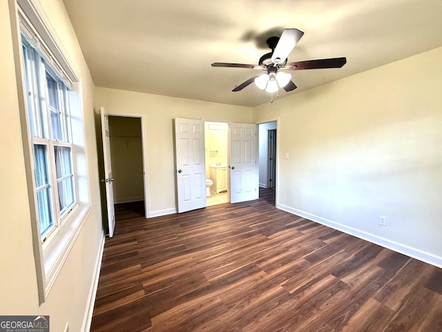 unfurnished bedroom with baseboards, connected bathroom, ceiling fan, dark wood-style flooring, and a walk in closet