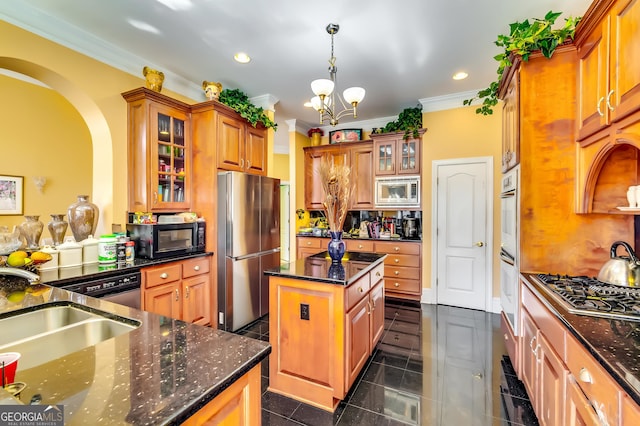 kitchen with brown cabinets, stainless steel appliances, dark stone countertops, and a center island