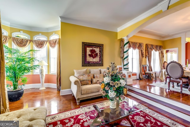 living area with decorative columns, baseboards, arched walkways, ornamental molding, and wood finished floors