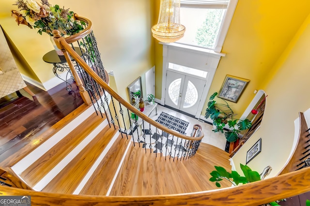 entrance foyer featuring a chandelier, wood finished floors, a towering ceiling, stairs, and french doors