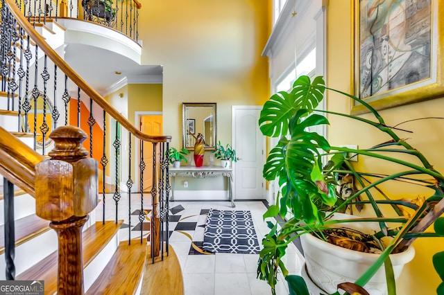 tiled entryway featuring baseboards, a high ceiling, ornamental molding, and stairs