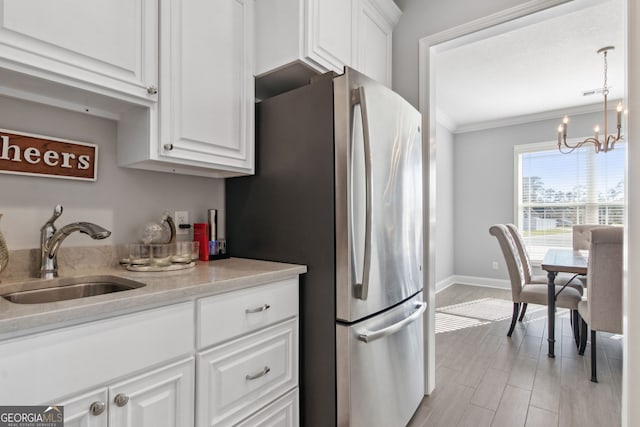 kitchen featuring crown molding, light countertops, freestanding refrigerator, white cabinetry, and a sink