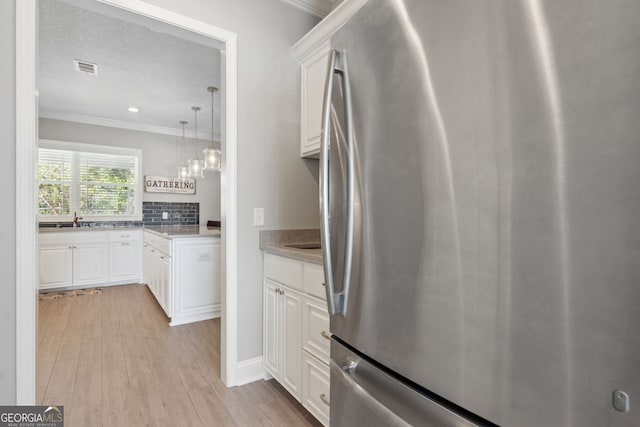 kitchen with light wood-style flooring, white cabinetry, freestanding refrigerator, and crown molding