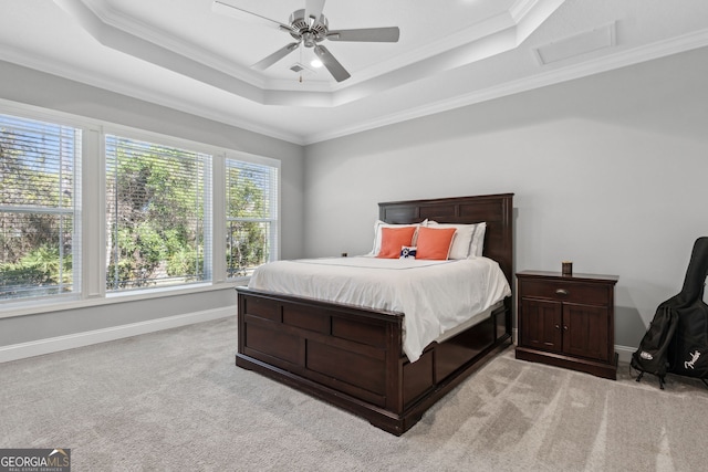 bedroom with ornamental molding, a tray ceiling, light colored carpet, and baseboards