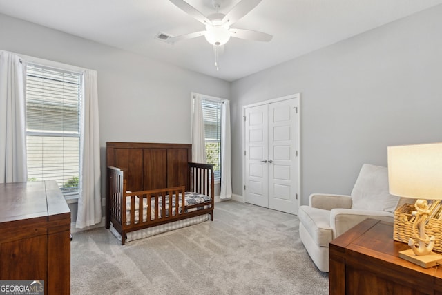 bedroom with a closet, light colored carpet, visible vents, ceiling fan, and baseboards