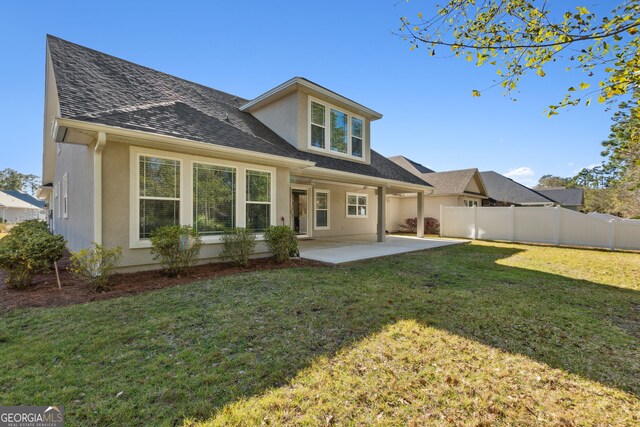 back of house featuring stucco siding, a shingled roof, a lawn, a patio area, and fence