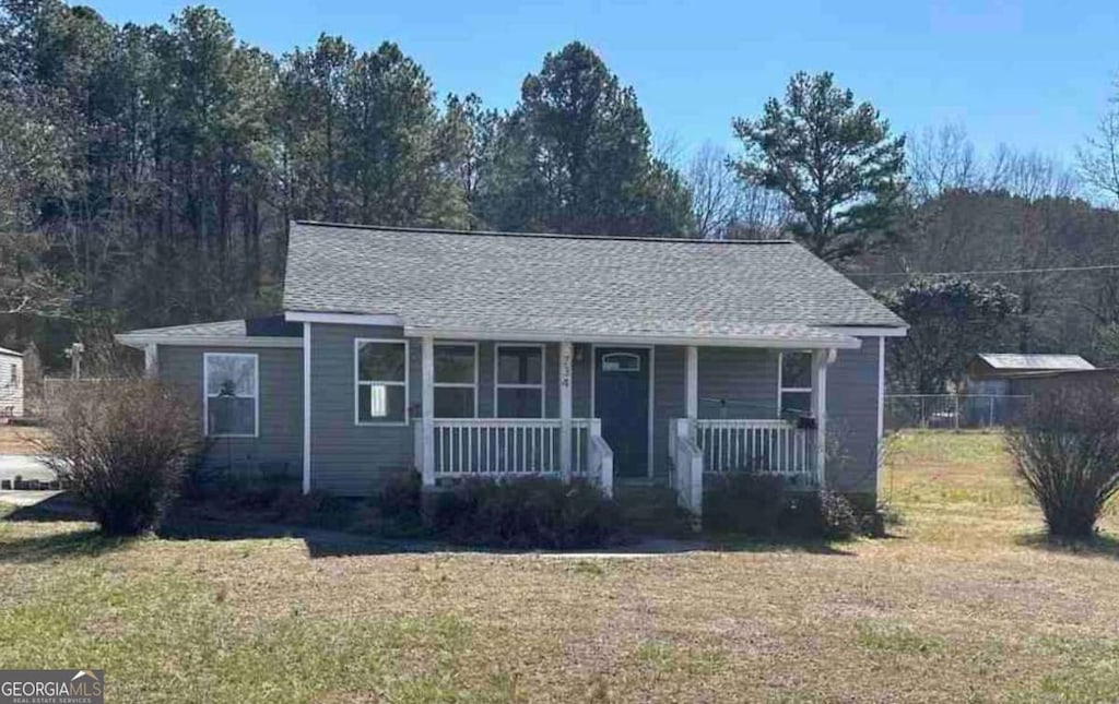 view of front of home with covered porch, a front lawn, and roof with shingles