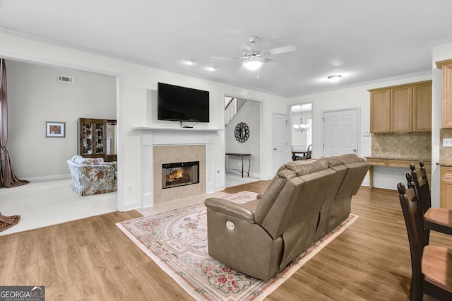 living room featuring ceiling fan with notable chandelier, a fireplace, visible vents, and crown molding